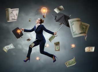 Entrepreneur in a suit walking under a storm of money and light bulbs, representing ideas.